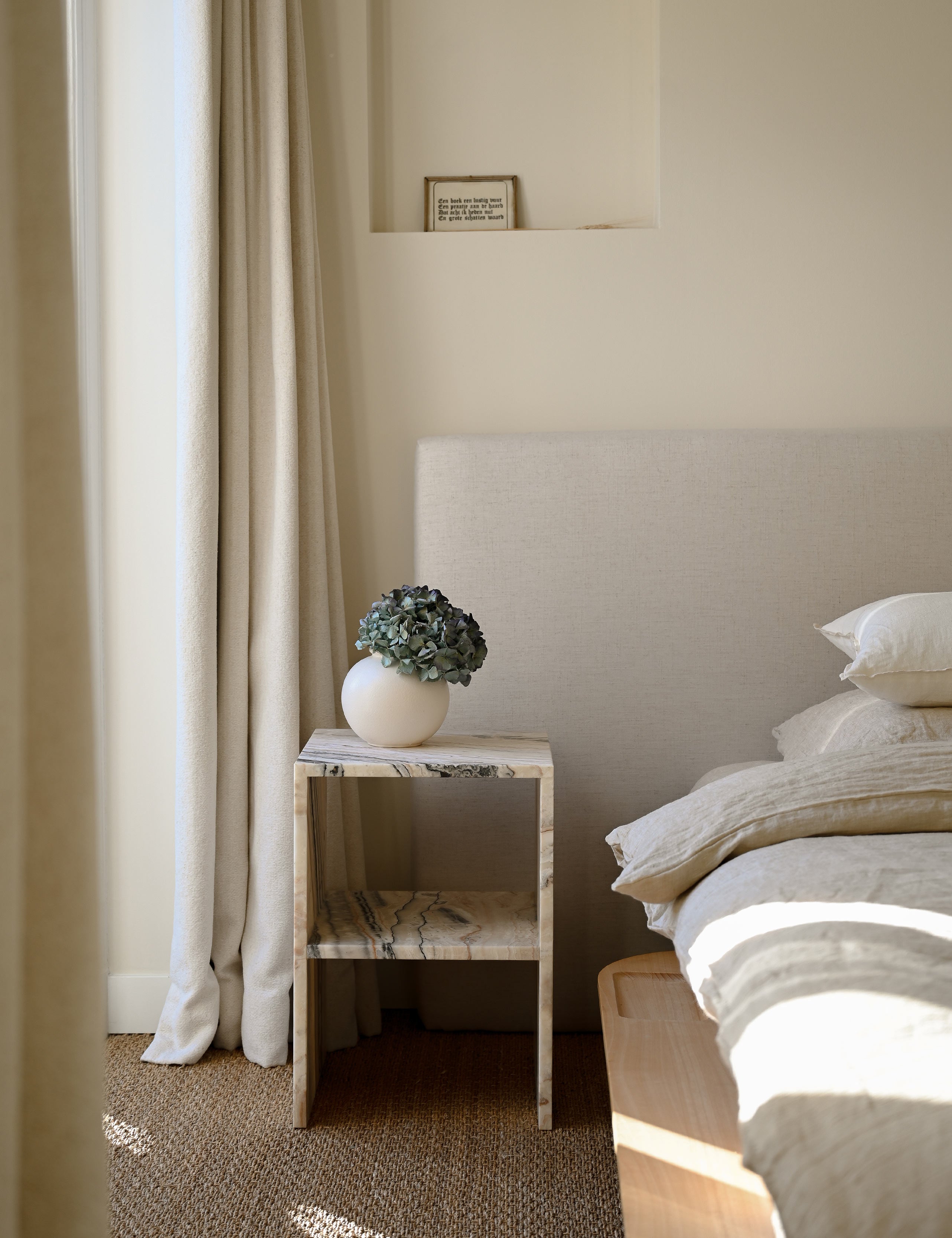 Interieur sfeerbeeld van elegant nachtkastje of bijzettafel gemaakt van natuursteen. Tijdloos in kwaliteit en stijl, in een hoekig design met opbergmogelijkheid. Uitgevoerd in een unieke en exclusieve onyx: desert linea, opvallend met diverse tinten beige en bruin.