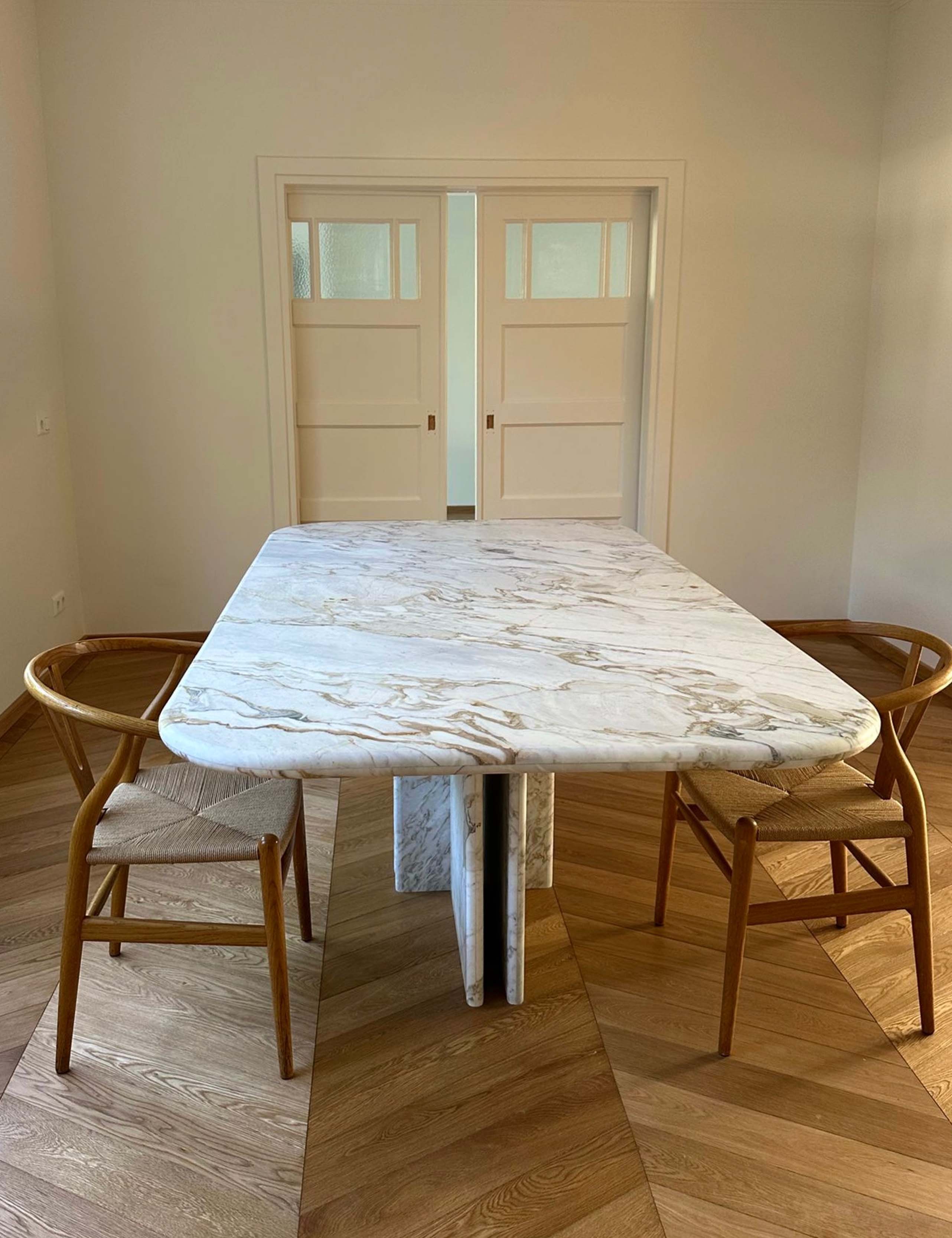 Marble dining table with rounded rectangular top and sculptural pedestal legs in a warm interior.