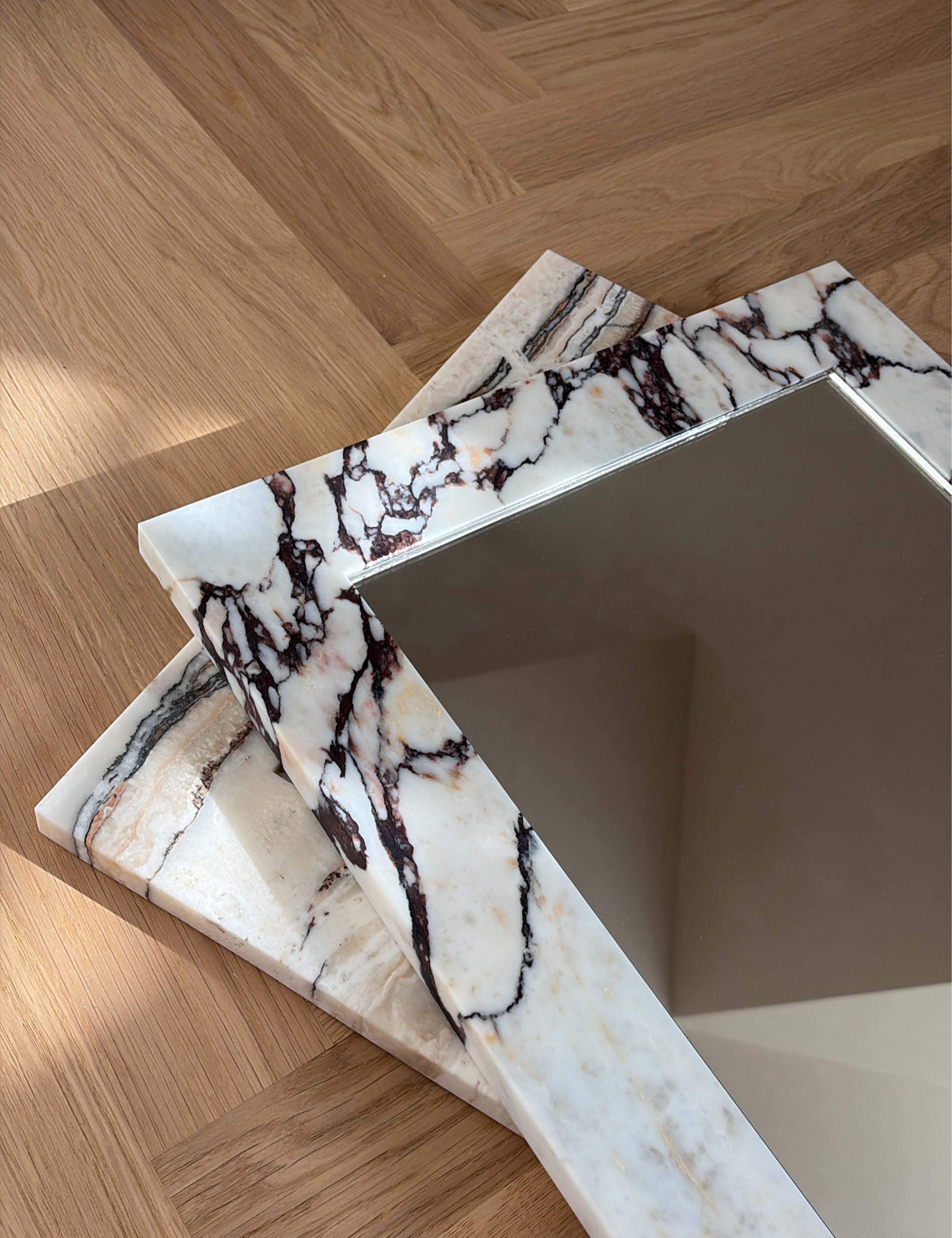 Detail of Opal Calacatta Viola marble mirror frame showing natural burgundy veining.