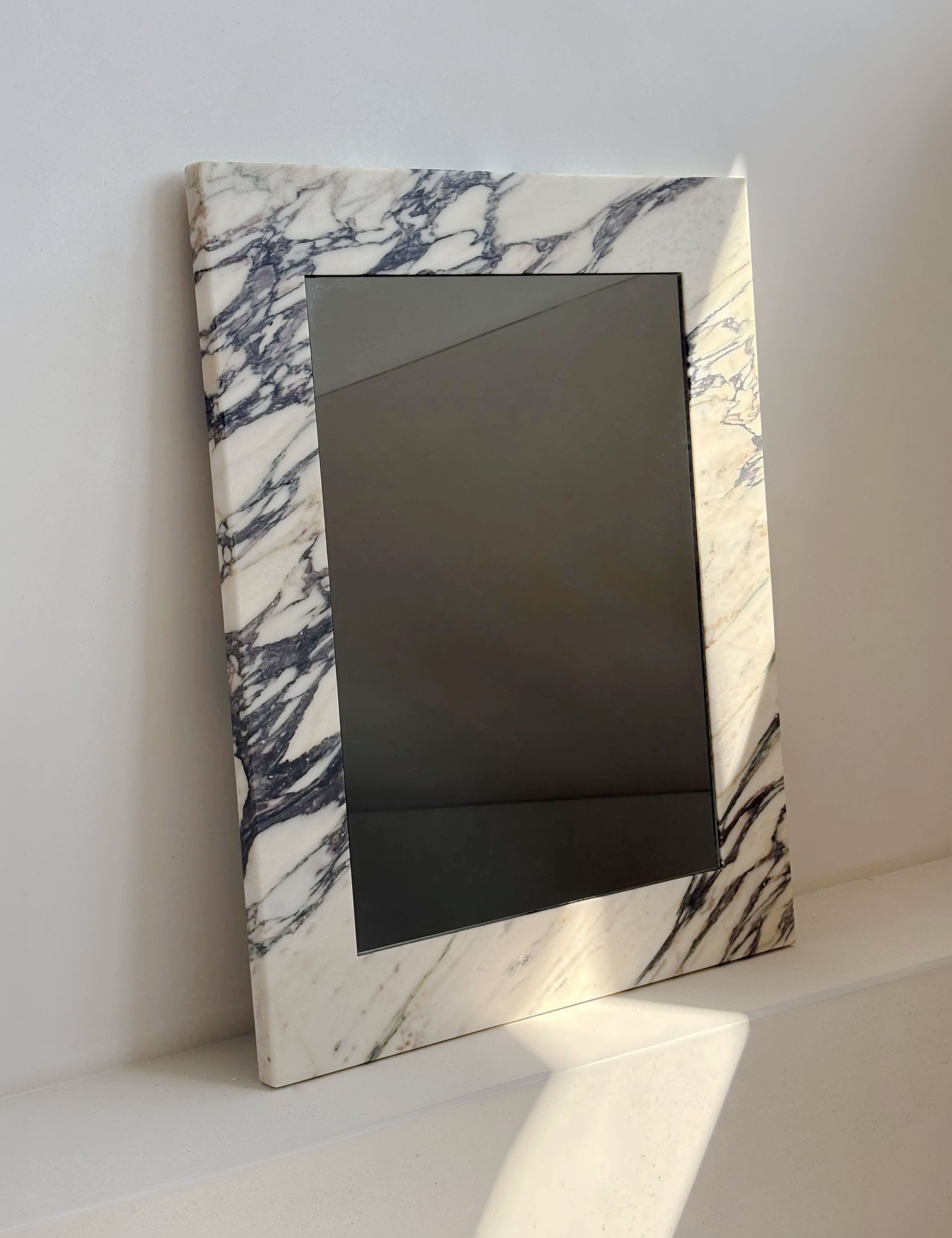 Opal Calacatta Viola marble mirror styled on a shelf with natural light highlighting the marble veining.
